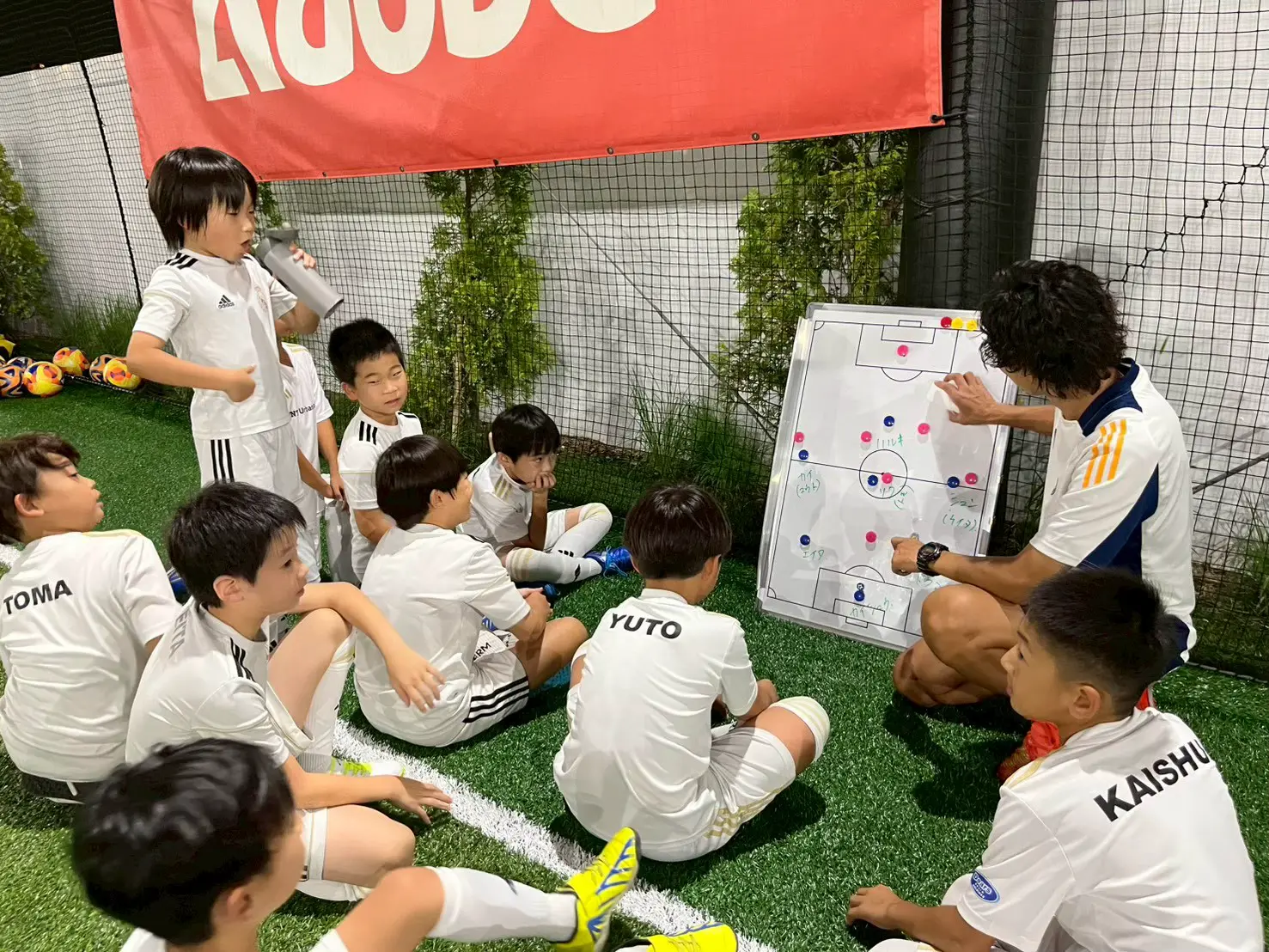 コーチが戦術ボードを使って、座って聞く子どもたちに説明している様子